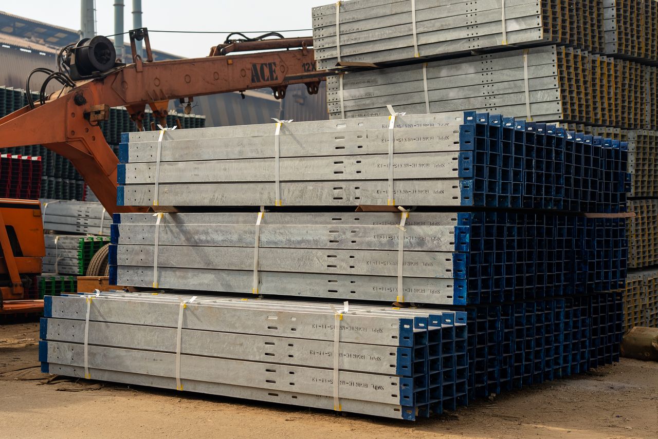 Stack of steel beams ready for construction in an industrial setting with crane.